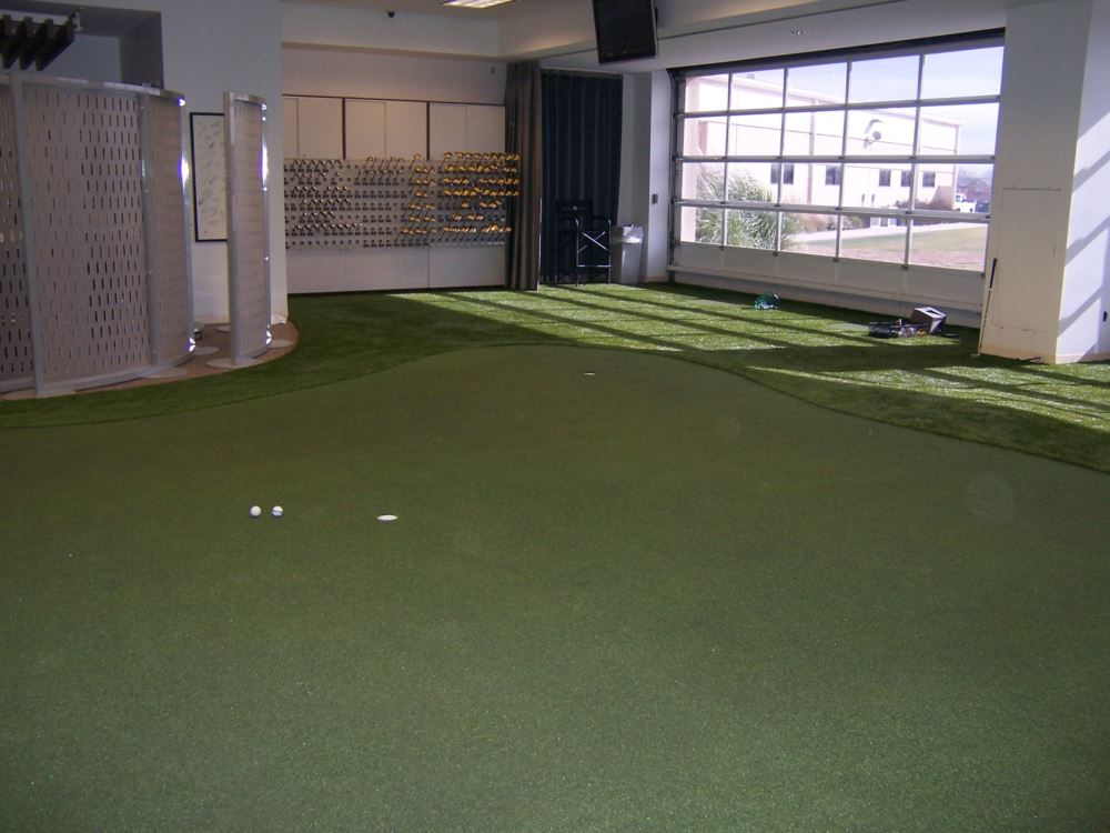 Professional indoor putting green with artificial turf and practice hole, installed inside a golf retail and fitting space for year-round training.