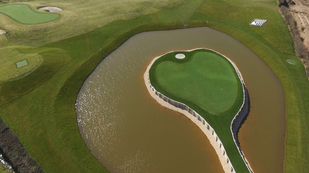Austin Aerial view of a vibrant green synthetic grass island in a natural pond on a golf course